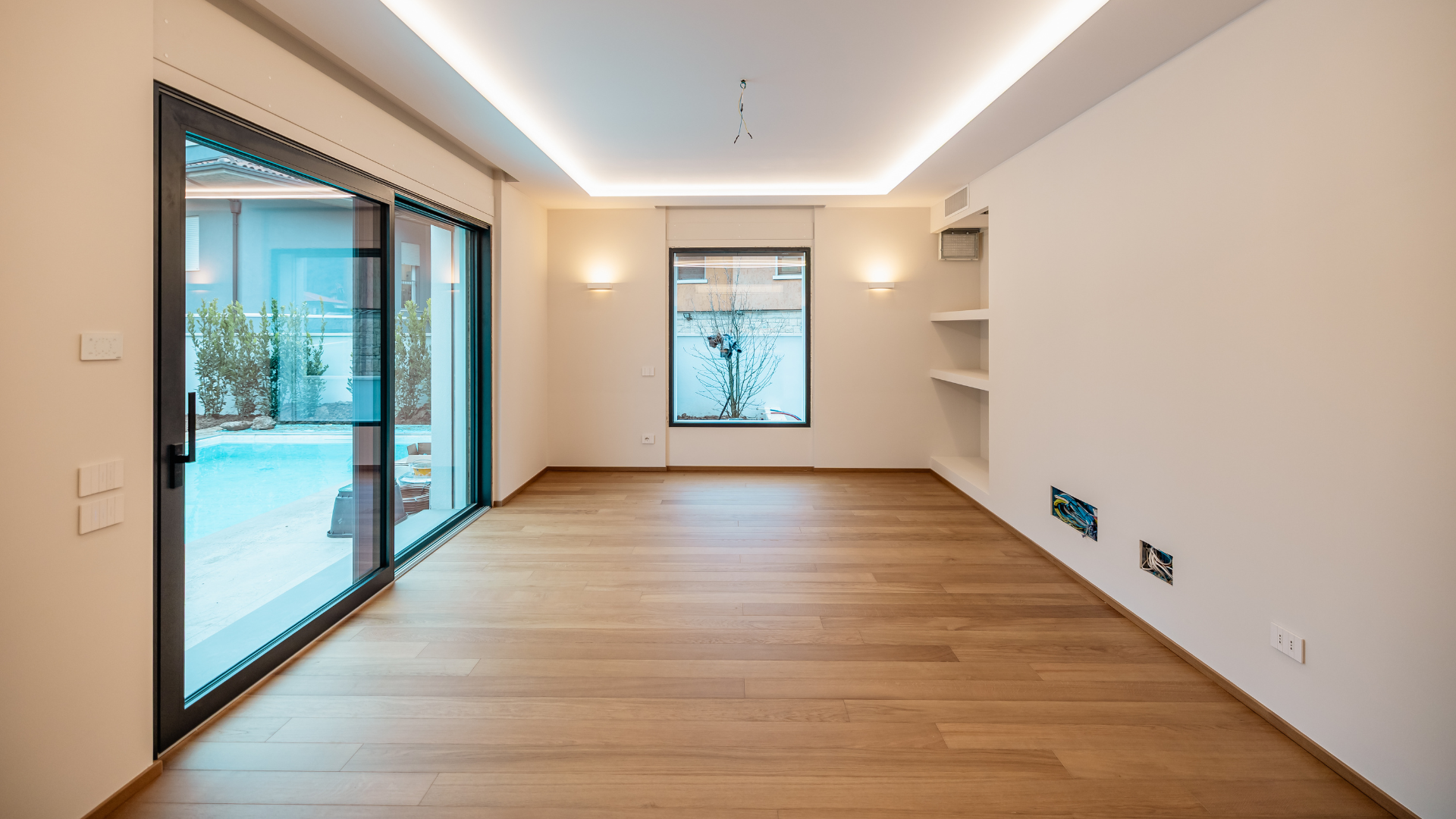 Ampio salone con riscaldamento a pavimento, gola luminosa a LED e vetrata scorrevole sulla piscina, mantenuto a temperatura ideale senza dispersioni termiche.