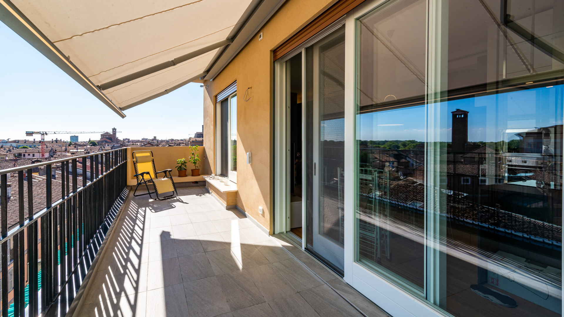 Ampio terrazzo panoramico con tenda da sole avvolgibile, pavimentazione in gres per esterni e vista sui tetti del centro urbano.