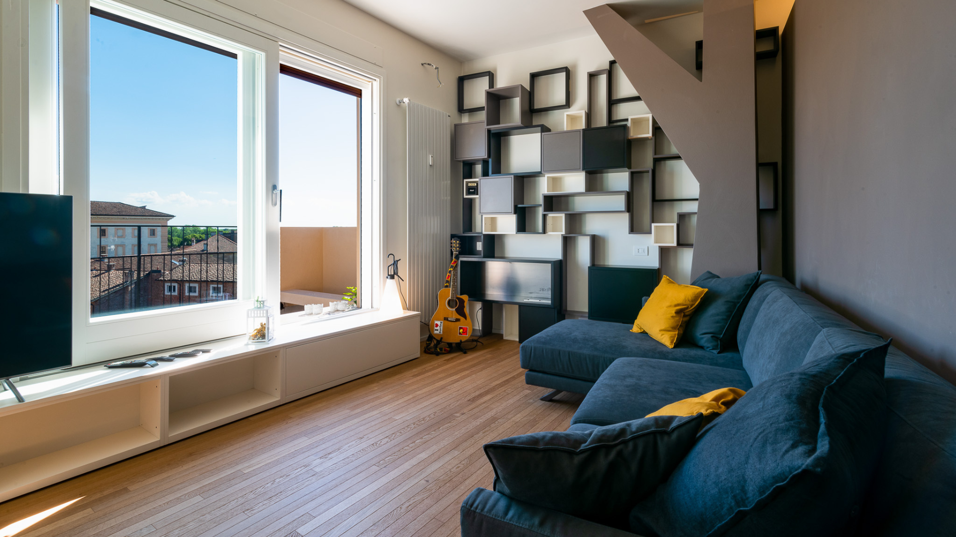 Silence, pure air, and relaxation: the ideal microclimate of a Casa Bianchetti Cozy living area with a blue sofa, yellow cushions, and a large window, where continuous air exchange ensures well-being, freedom from pollen, and insulation from external noise.