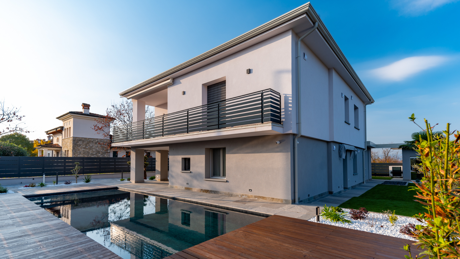 Prospetto esterno di una villa moderna a due piani con piscina interrata, decking in legno e giardino privato.