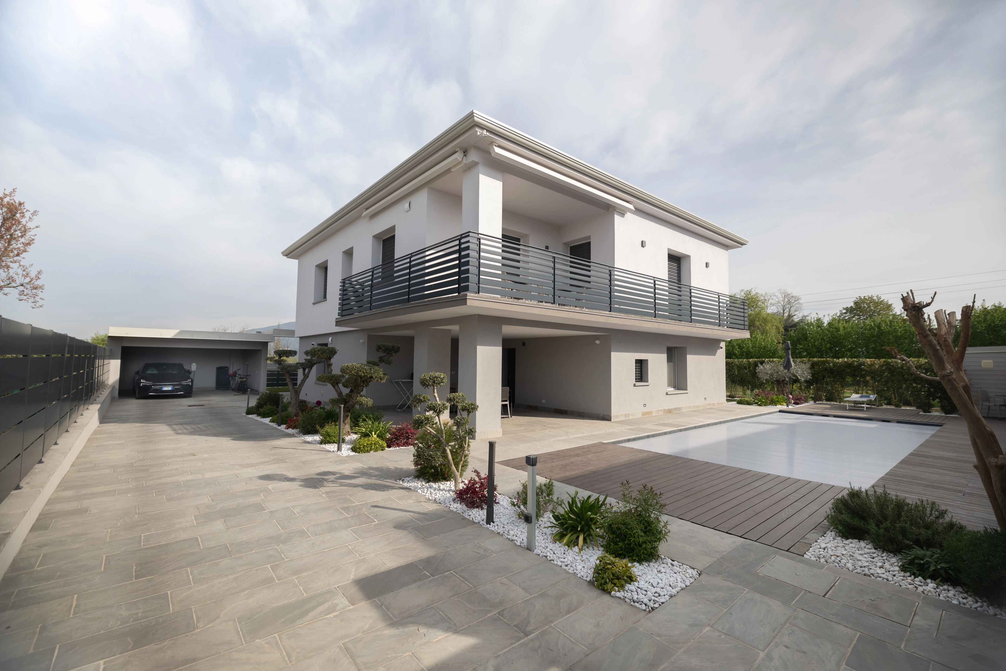 Esterno di una villa moderna minimalista a due piani con piscina interrata, pavimentazione in legno per l'outdoor e giardino di design curato da Bianchetti.